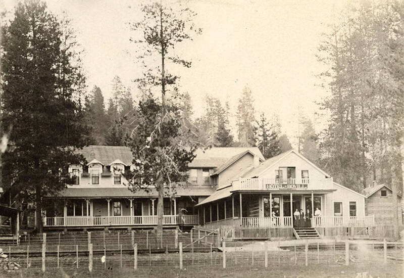 Women stand on the front porch of the Bovill Hotel, surrounded by trees.