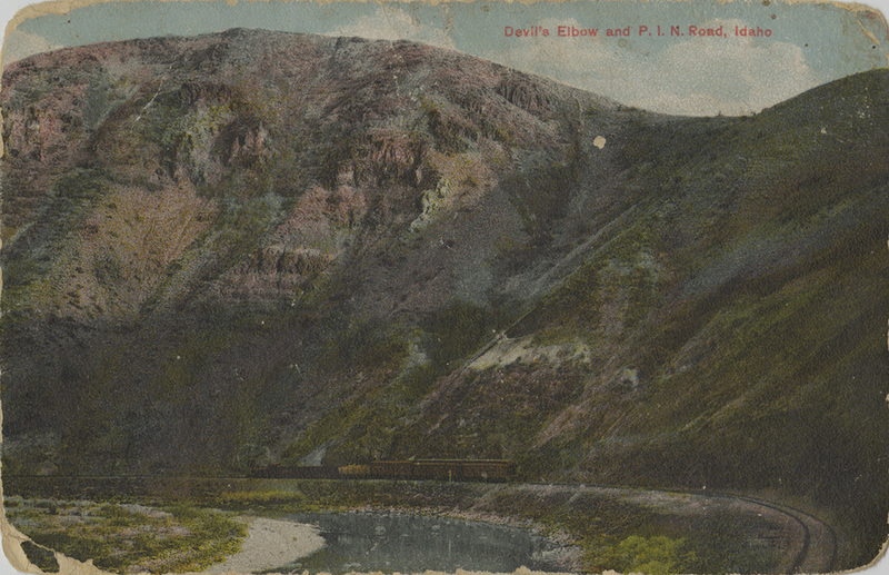 Postcard of a train travelling around a sharp corner near Wallace, Idaho.
