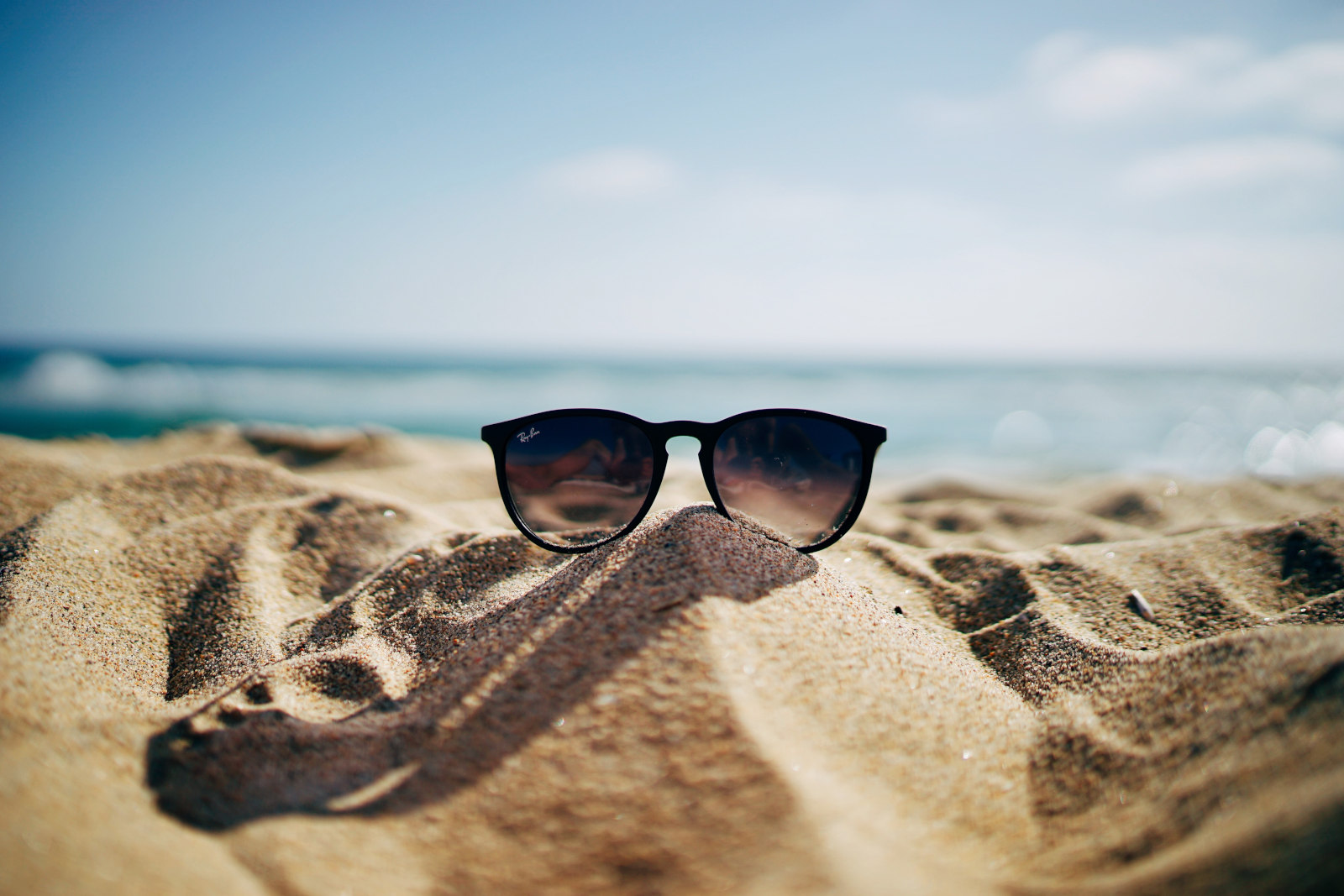 a pair of sunglasses sitting on the sand at the beach