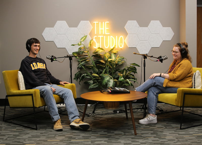 two people with microphones with a neon sign saying The Studio