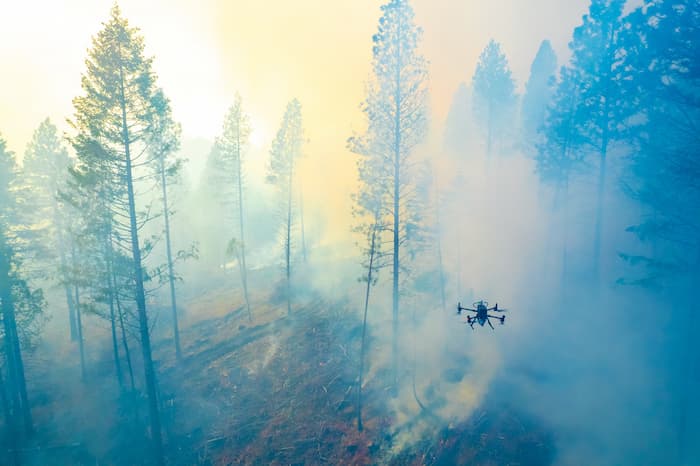 a drone flies above a smoldering wildfire