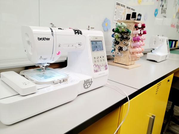 white sewing machine next to holder full of thread